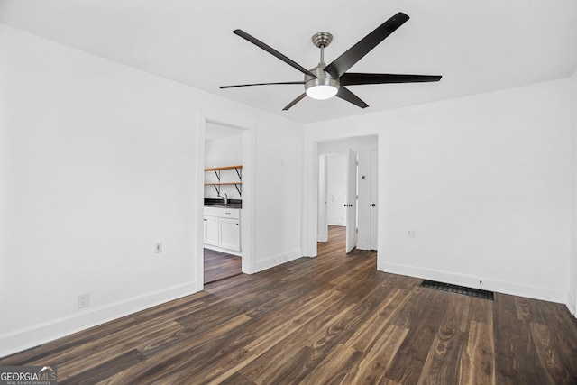 unfurnished room with a sink, ceiling fan, baseboards, and dark wood-type flooring