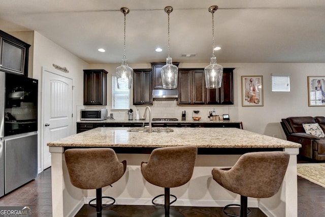 kitchen with light stone counters, a sink, a kitchen breakfast bar, and appliances with stainless steel finishes
