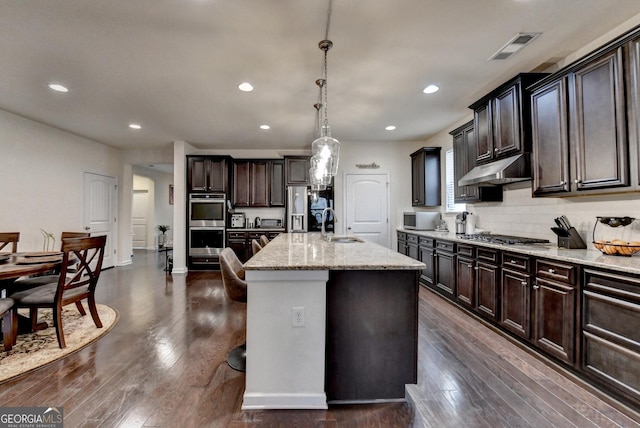 kitchen featuring visible vents, light stone countertops, dark wood-style floors, under cabinet range hood, and stainless steel appliances