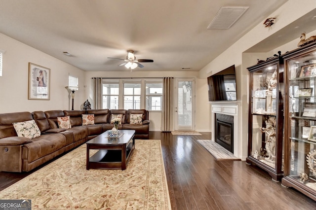living room featuring dark wood-style flooring, a fireplace, a ceiling fan, baseboards, and visible vents