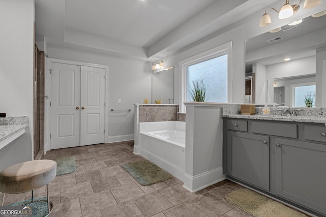 full bathroom featuring baseboards, a bath, a tray ceiling, vanity, and a wealth of natural light