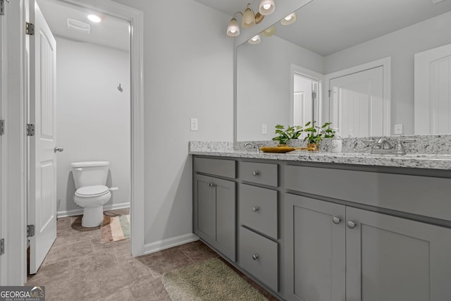 bathroom with double vanity, baseboards, visible vents, toilet, and a sink