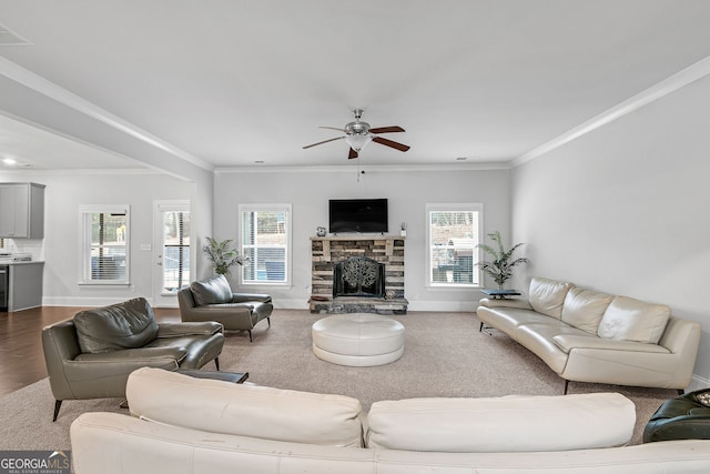 living room with ornamental molding, a stone fireplace, baseboards, and a ceiling fan