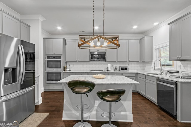 kitchen featuring crown molding, gray cabinetry, appliances with stainless steel finishes, a sink, and a kitchen island
