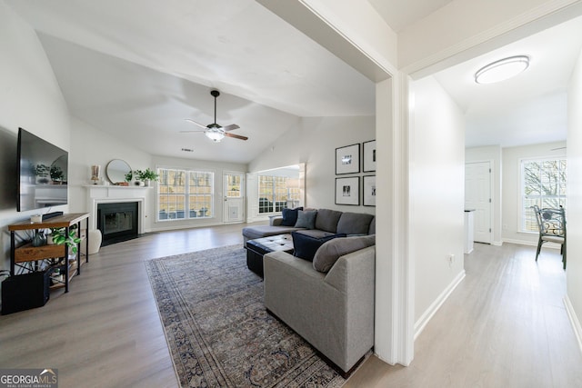 living room with lofted ceiling, plenty of natural light, a fireplace with flush hearth, and light wood-style floors