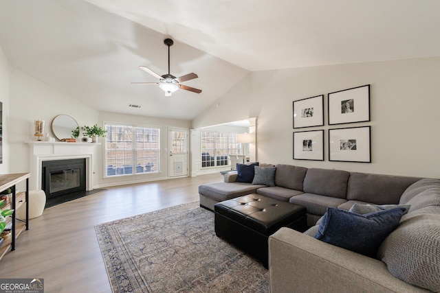 living room with a fireplace with flush hearth, visible vents, a ceiling fan, vaulted ceiling, and light wood-type flooring