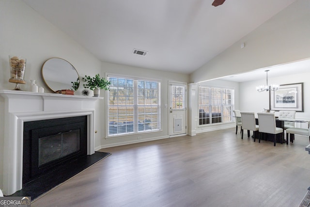 living area with lofted ceiling, visible vents, a glass covered fireplace, wood finished floors, and baseboards