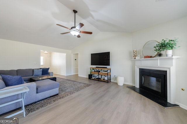 living area with baseboards, a ceiling fan, a glass covered fireplace, lofted ceiling, and wood finished floors