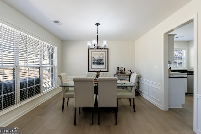 dining space featuring visible vents, a chandelier, wood finished floors, and a decorative wall