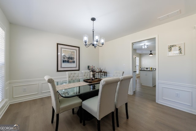 dining room with a chandelier, a decorative wall, a wainscoted wall, wood finished floors, and visible vents