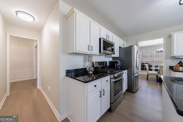 kitchen featuring baseboards, dark stone countertops, stainless steel appliances, light wood-type flooring, and white cabinetry