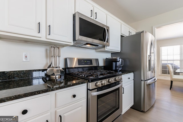 kitchen featuring light wood-type flooring, white cabinetry, stainless steel appliances, and dark stone countertops