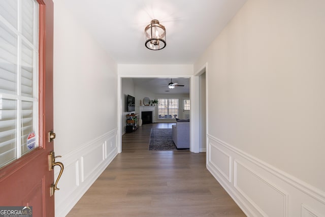 hall with a notable chandelier, wainscoting, light wood-type flooring, and a decorative wall