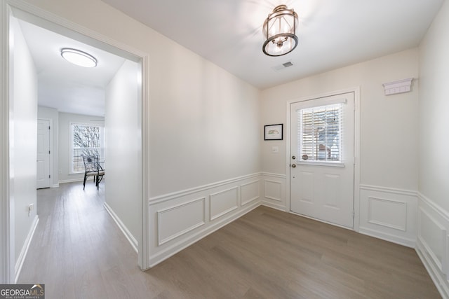 entryway with a wainscoted wall, wood finished floors, visible vents, and a decorative wall