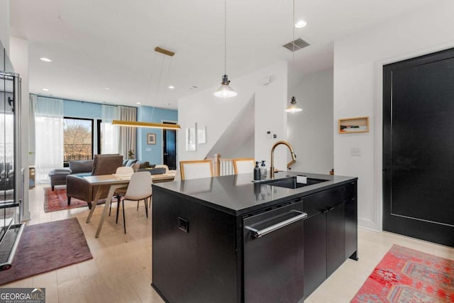 kitchen with dark cabinets, a sink, visible vents, dark countertops, and a center island with sink