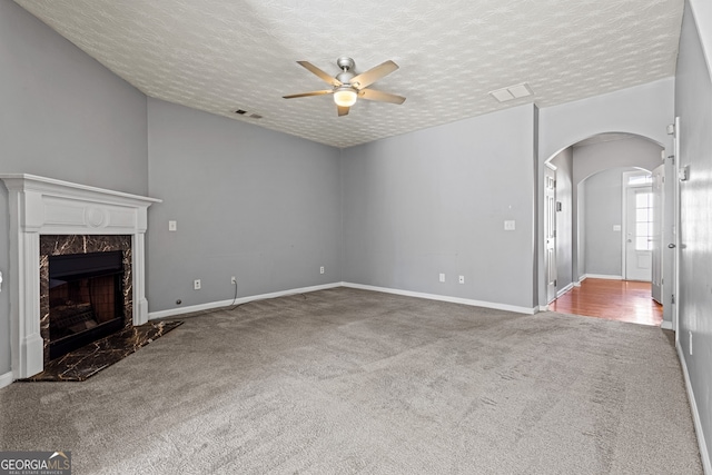 unfurnished living room with arched walkways, a fireplace, visible vents, a ceiling fan, and carpet flooring