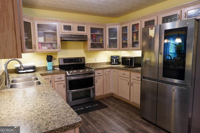 kitchen with a textured ceiling, under cabinet range hood, a sink, appliances with stainless steel finishes, and dark wood finished floors