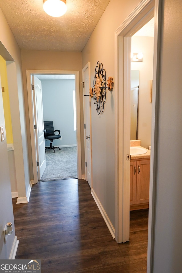 hall with a textured ceiling, baseboards, and dark wood-type flooring