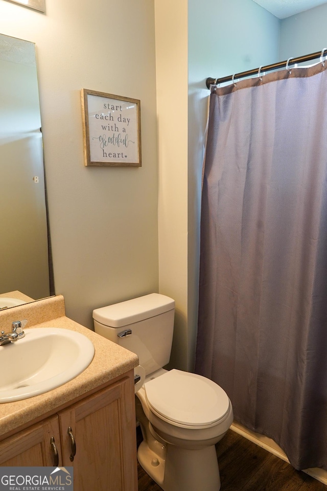 bathroom featuring wood finished floors, vanity, toilet, and curtained shower