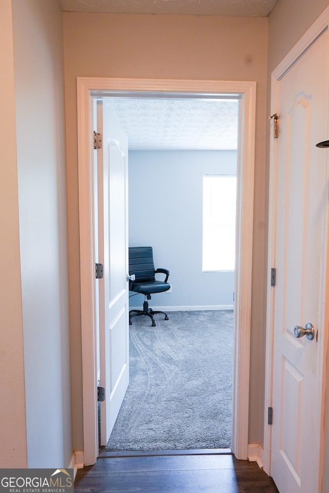 hallway featuring baseboards and dark carpet