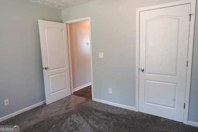 unfurnished bedroom with a textured ceiling, dark colored carpet, and baseboards