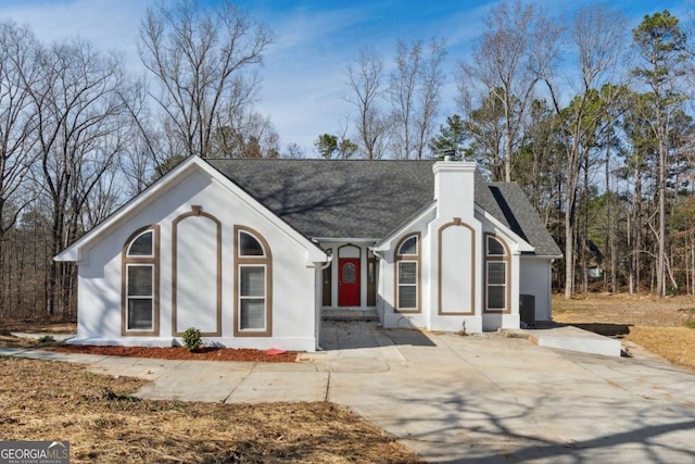 view of front facade featuring roof with shingles, a chimney, and stucco siding