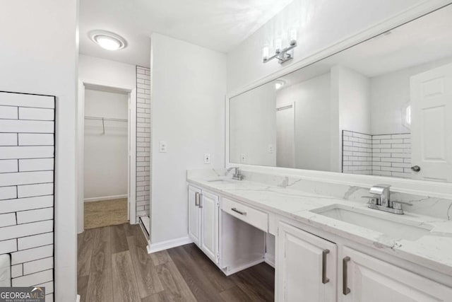 bathroom with double vanity, a spacious closet, a sink, and wood finished floors