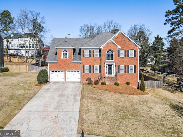 colonial home with a garage, brick siding, fence, and a front lawn