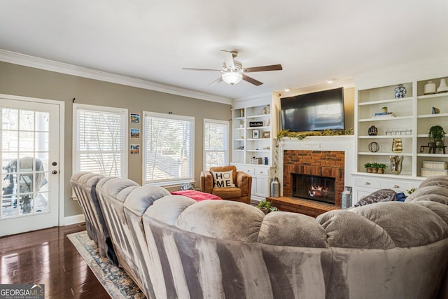 living area with built in shelves, a brick fireplace, dark wood finished floors, and crown molding