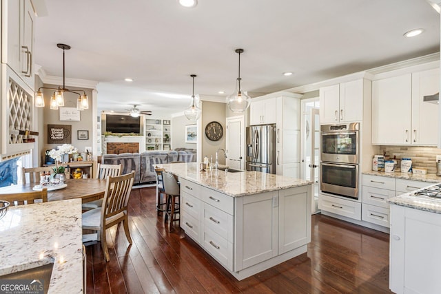 kitchen featuring dark wood finished floors, appliances with stainless steel finishes, ornamental molding, a fireplace, and a sink