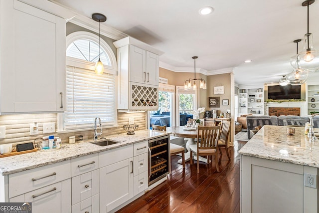 kitchen with dark wood-style floors, a fireplace, ornamental molding, a sink, and beverage cooler