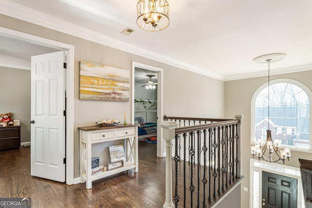 corridor with visible vents, dark wood finished floors, an inviting chandelier, crown molding, and an upstairs landing