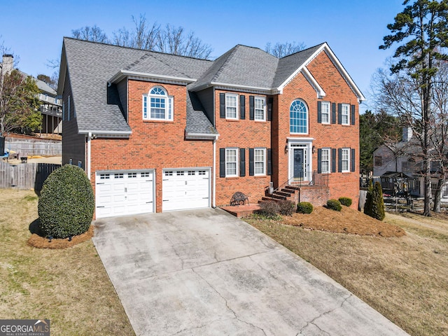 colonial inspired home featuring a shingled roof, brick siding, fence, and driveway