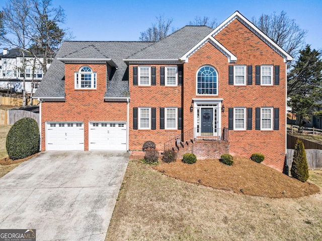 colonial home with a garage, brick siding, fence, concrete driveway, and roof with shingles