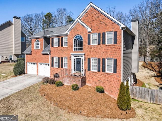 colonial house with brick siding, a chimney, an attached garage, fence, and driveway