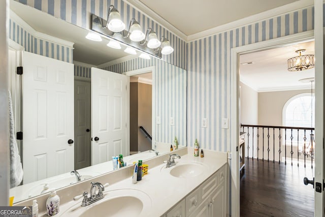 bathroom with ornamental molding, a chandelier, a sink, and wallpapered walls