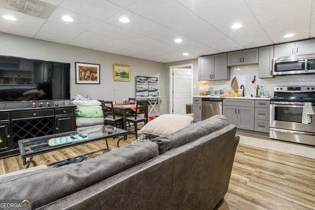 living room with a paneled ceiling, light wood-type flooring, visible vents, and recessed lighting