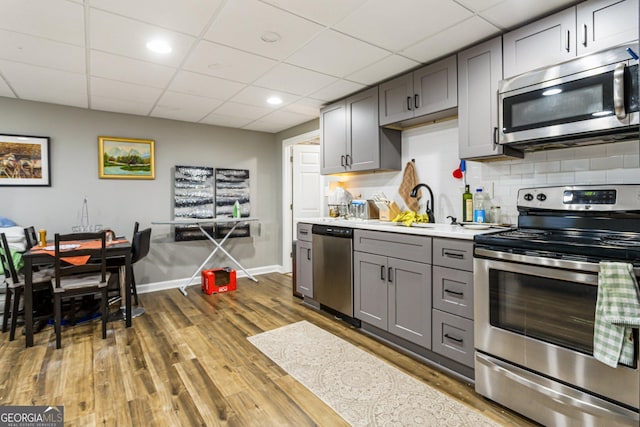 kitchen with stainless steel appliances, tasteful backsplash, light countertops, gray cabinetry, and wood finished floors