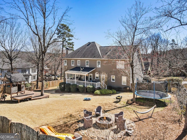 back of property with a deck, a fire pit, fence, a trampoline, and a chimney