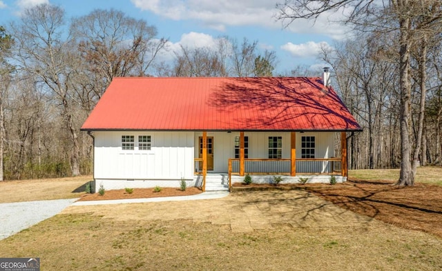 view of front of home with metal roof, a porch, board and batten siding, a front lawn, and a chimney