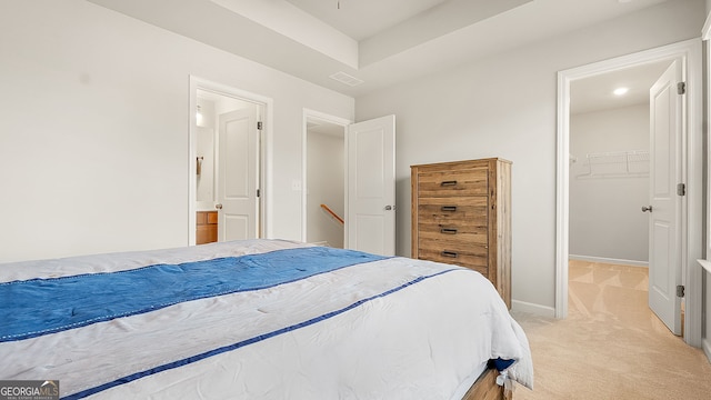 bedroom with light colored carpet, visible vents, baseboards, a walk in closet, and ensuite bath