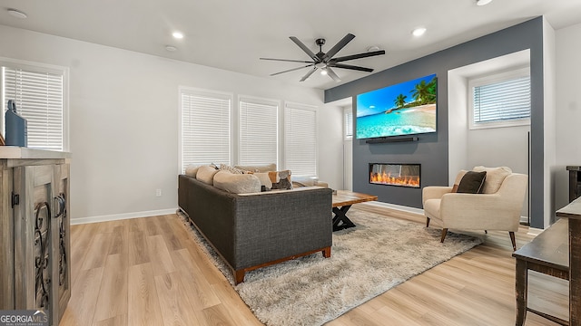 living area with light wood-style floors, a glass covered fireplace, ceiling fan, and baseboards