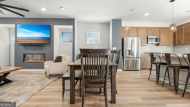 dining space with light wood-type flooring, a glass covered fireplace, a ceiling fan, and recessed lighting