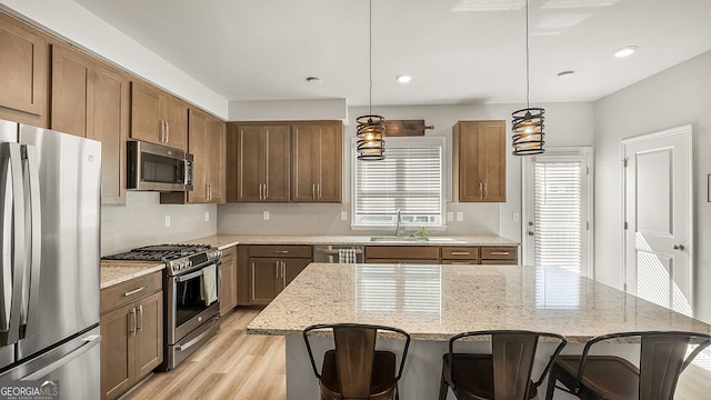 kitchen featuring stainless steel appliances, decorative backsplash, a sink, light stone countertops, and light wood-type flooring