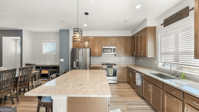 kitchen with light stone counters, stainless steel appliances, a sink, a center island, and decorative backsplash