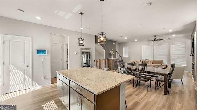 kitchen with baseboards, light wood-style flooring, a kitchen island, light stone counters, and hanging light fixtures