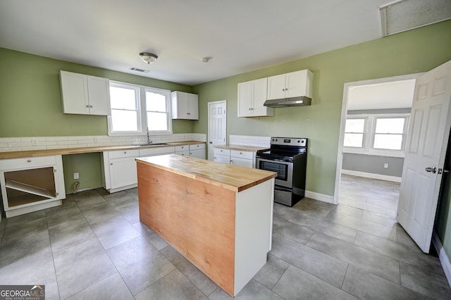 kitchen with a sink, under cabinet range hood, stainless steel electric range, white cabinets, and wooden counters