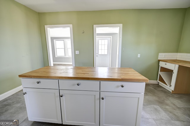 kitchen featuring white cabinetry, light tile patterned flooring, baseboards, and butcher block countertops