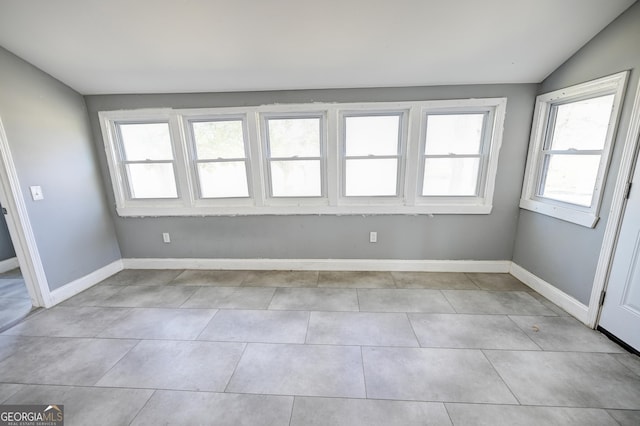 unfurnished room with light tile patterned floors, baseboards, and vaulted ceiling