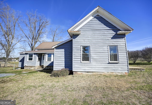 rear view of property featuring a lawn and metal roof